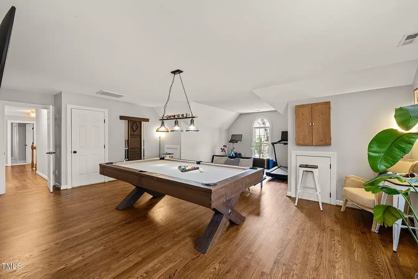 The far end of the finished attic with a pool table, arched window and hardwood floor