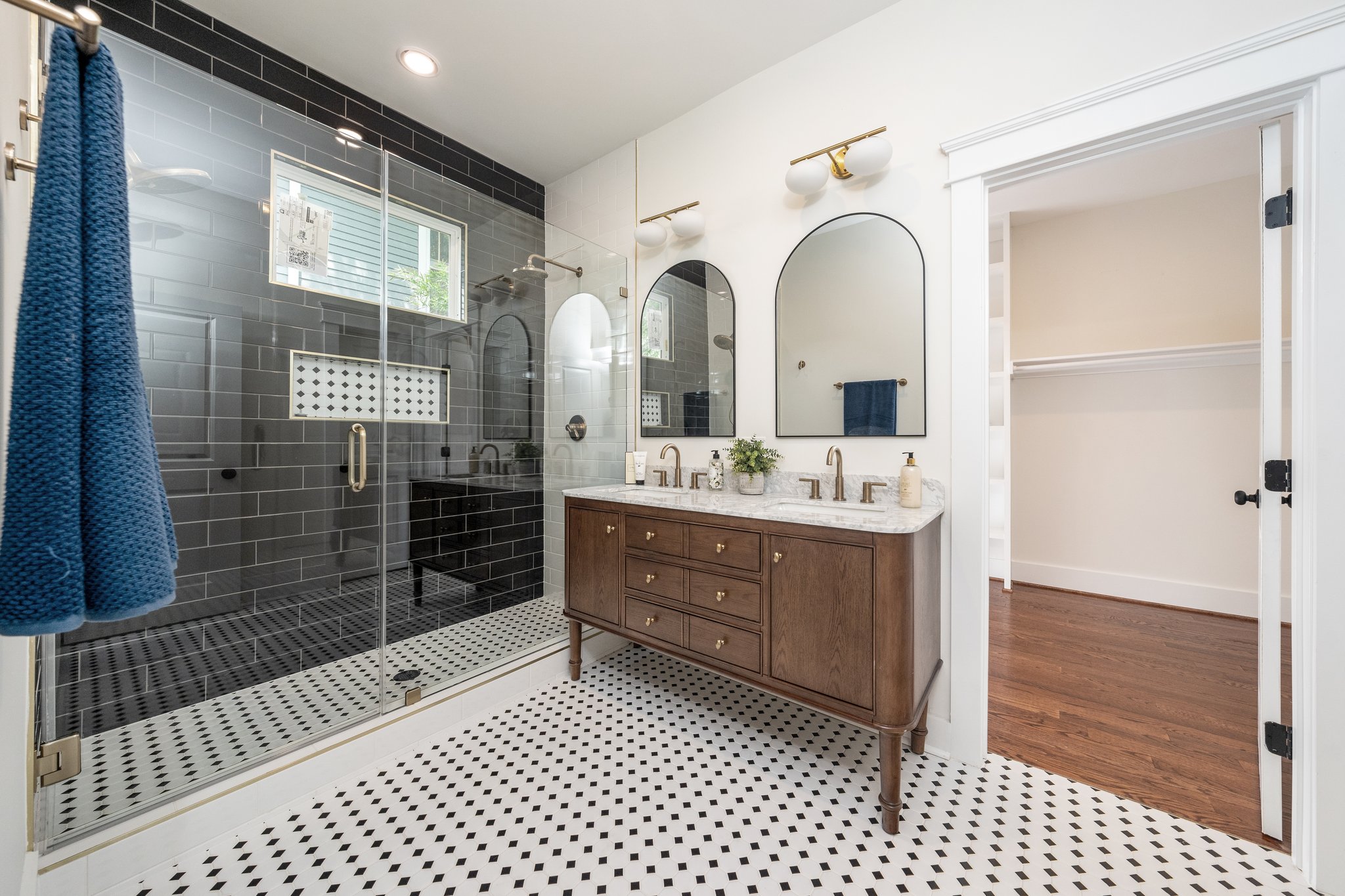 Bathroom with a grey tiled walk-in shower, black and white mosaic floor and a wood double vanity